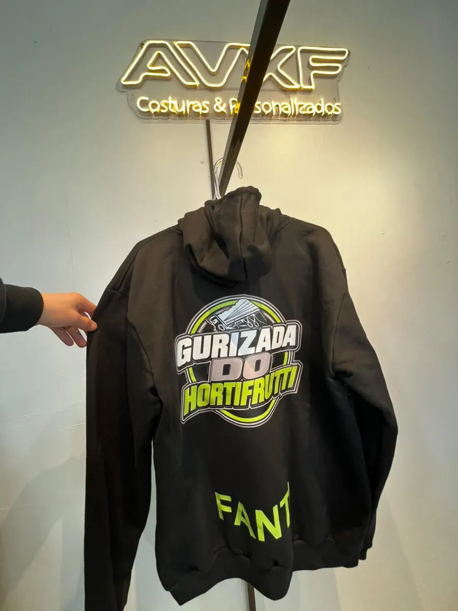 Moletom preto personalizado com a estampa Gurizada do Hortifrutti, pendurado em frente ao letreiro neon da AVXF